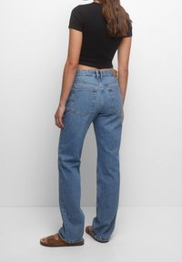 Jean en denim bleu taille haute à coupe décontractée, avec poches arrière en patch et étiquette en cuir à la taille, associé à un haut noir ajusté.