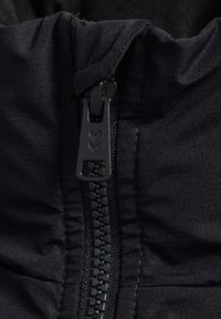 Sort stof med lynlåslukning, der har en mat tekstur og synlige syninger. Lynlåsen har et slankt design og en trækflig med pilemønster.