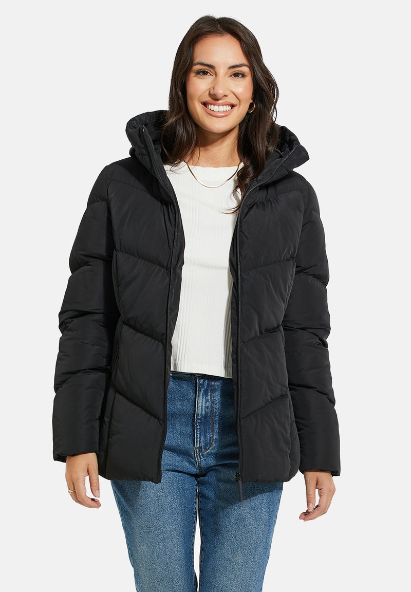 Svart puffjacka med huva, med en quiltad design, dragkedjestängning och sidofickor, som bärs över en vit topp och blå jeans.