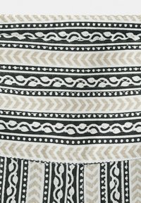 Rayures horizontales et verticales noires et beiges avec motifs chevrons et tourbillons ponctués sur le tissu.