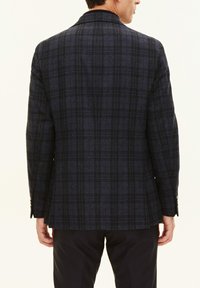 Mörk rutig kavaj med en ulltextur, som har blå och grå nyanser. Anmärkningsvärda detaljer inkluderar en notch-krage och en enda bakventil.