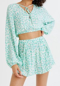 Dwuczęściowy strój składający się z krótko skrojonego topu i dopasowanych szortów, z jasnoturkusowym, kwiatowym wzorem, elastycznym pasem i ozdobnymi wiązaniami.