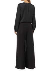 Schwarze Satin-Bluse mit langen Ärmeln, kombiniert mit weit geschnittenen schwarzen Hosen, die eine glatte Textur und einen schlichten Rundhalsausschnitt aufweisen.