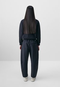 Temno modra sweatshirt s sproščenim krojem in dolgimi rokavi, v kombinaciji z ujemajočimi se ožjimi hlačami. Material se zdi mehak, teksturiran in brez okraskov.
