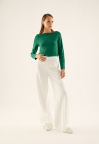 Groene langemouwen top met een bootnek, gecombineerd met hoge taille witte wijdere broeken. Gestructureerde stof en een soepele silhouet.