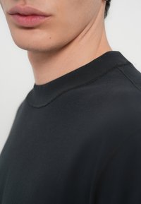 Μαύρο φούτερ με στρογγυλή λαιμόκοψη από απαλό ύφασμα, που φαίνεται να έχει λείο υφή και καθαρές άκρες με ελάχιστες ραφές.