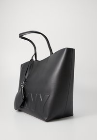 Black leather tote bag with embossed "NY" logo, elongated design, dual handles, and a detachable small pouch with zipper.