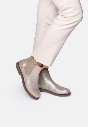 Metallic gold Chelsea boots with elastic side panels, a smooth texture, and a slim brown rubber sole. Paired with light-colored pants.