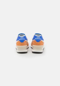 Sneakers med en överdel i främst orange mocka, blå accenter och vita detaljer. Har en dämpad sula och en kontrasterande svart yttersula.