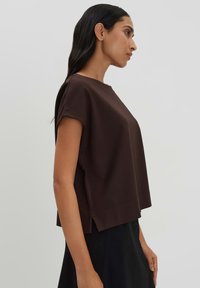 Braunes, kurzärmliges Oberteil mit lockerer Passform, Rundhalsausschnitt und seitlichen Schlitzen. Glattes Material mit matter Optik und minimalistischem Design.