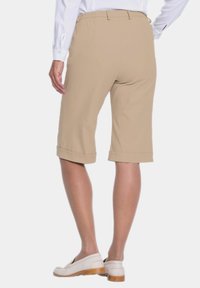 Shorts beige à mi-cuisses en tissu lisse, avec un ourlet roulé et une taille élastiquée. Associés à des chaussures de couleur claire.