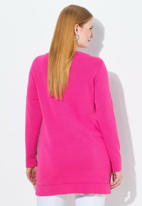 Túnica de manga larga en rosa brillante, hecha de una tela suave. Presenta un escote redondo, aberturas laterales y un corte relajado para mayor comodidad.