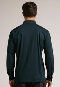 Langarmhemd in dunklem Petrol, aus glattem Stoff gefertigt. Verfügt über einen klassischen Kragen und knöpfbare Manschetten sowie einen geraden Saum.