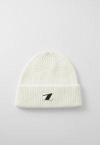 Bonnet tricoté blanc avec un design côtelé, un revers et une patch logo noir et blanc sur le devant.