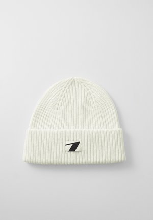 Bonnet tricoté blanc avec un design côtelé, un revers et une patch logo noir et blanc sur le devant.