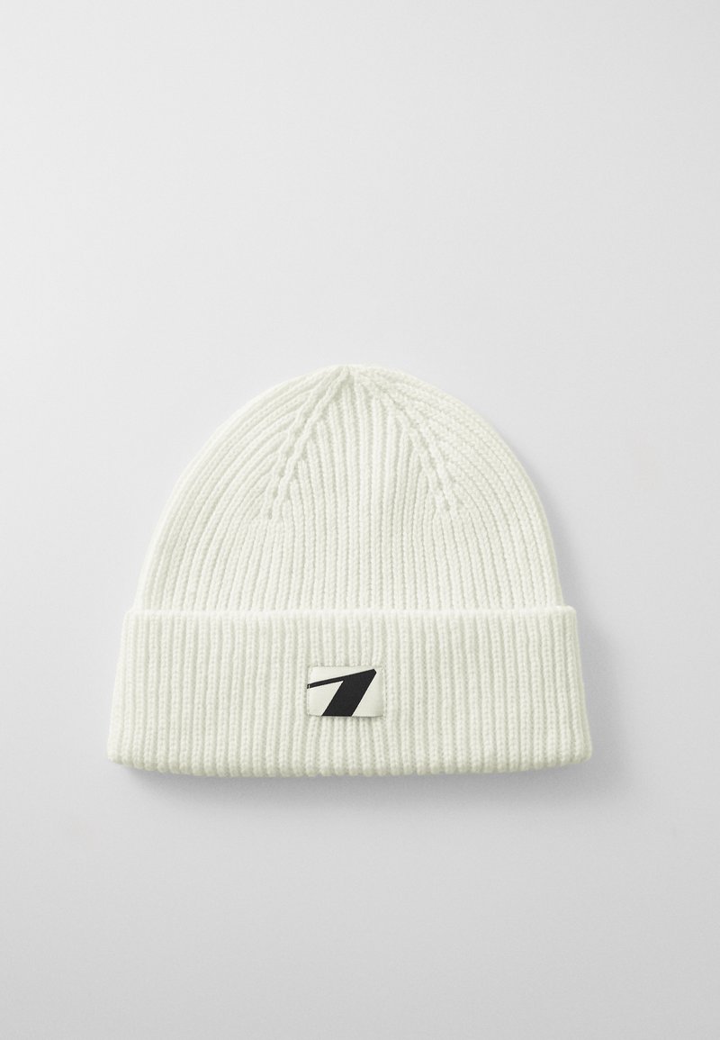 Bonnet tricoté blanc avec un design côtelé, un revers et une patch logo noir et blanc sur le devant.