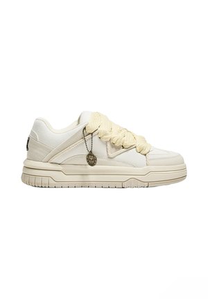 White sneakers with textured leather, thick beige laces, and a round charm accent. Low-top design with a ridged sole.