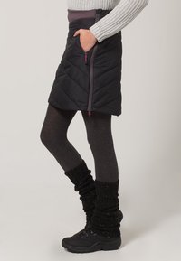 Padded černá zateplená sukně se bočním zipem, šedý pas, nošena přes šedé punčochy, doplněna černými kotníkovými botami a pletenými návleky na nohy.