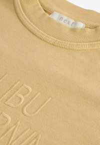 Žlutá mikina s žebrovaným kulatým výstřihem, s vyvýšeným vyšitým textem. Měkká textura a bezšvová konstrukce pro pohodlí.