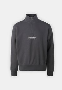 Felpa grigia scura con zip a un quarto, maniche lunghe e testo bianco "originals Studio" sul petto, mostrata su uno sfondo chiaro e semplice.