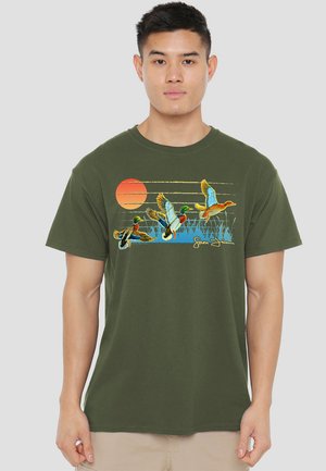 Olivgrünes Baumwoll-T-Shirt mit einem grafischen Motiv von fliegenden Enten vor einem Sonnenuntergangshintergrund. Mit kurzen Ärmeln und klassischem Rundhalsausschnitt.