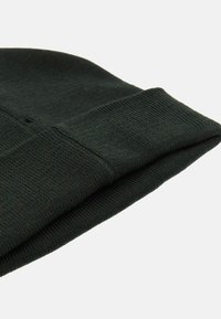 Beanie lavorato a maglia di un verde scuro con risvolto. Realizzato in un morbido tessuto testurizzato con un motivo a maglia aderente e costruzione senza cuciture.