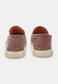 Braune Wildleder-Slipper mit flacher Profil und cremefarbenen Gummisohlen. Die Rückseite hat eine weiche, abgerundete Ferse. Keine sichtbare Markenkennzeichnung.