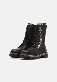 Botas de combate de cuero negro con cordones en la parte delantera, decoradas con acentos de rhinestones florales en el lado exterior y una suela de goma resistente.