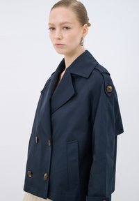 Marinblå dubbelknäppt trenchcoat med stora kragar, bruna knappar och sidofickor; har en avslappnad passform och en mjuk textur.