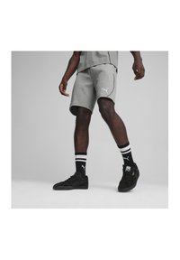 Graue Sportshorts mit einem kontrastierenden weißen Logo, kombiniert mit schwarzen Schuhen und gestreiften Socken, die einen lässigen Sportlook präsentieren.