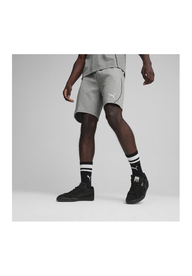 Graue Sportshorts mit einem kontrastierenden weißen Logo, kombiniert mit schwarzen Schuhen und gestreiften Socken, die einen lässigen Sportlook präsentieren.