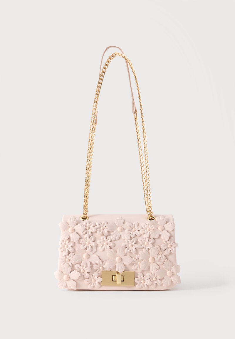 Pequeño bolso de mano rosa pálido con un patrón floral en relieve, cierre rectangular dorado y una larga correa de cadena dorada sobre un fondo blanco.