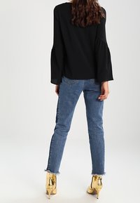 Blusa nera a maniche lunghe con maniche larghe, abbinata a jeans di denim blu con orlo grezzo e scarpe con tacco alto dorate.