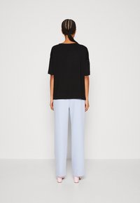 Černé oversized tričko s krátkými rukávy spojené se světle modrými širokými kalhotami a růžovými botami na blokovém podpatku. Jednoduchý, čistý design.