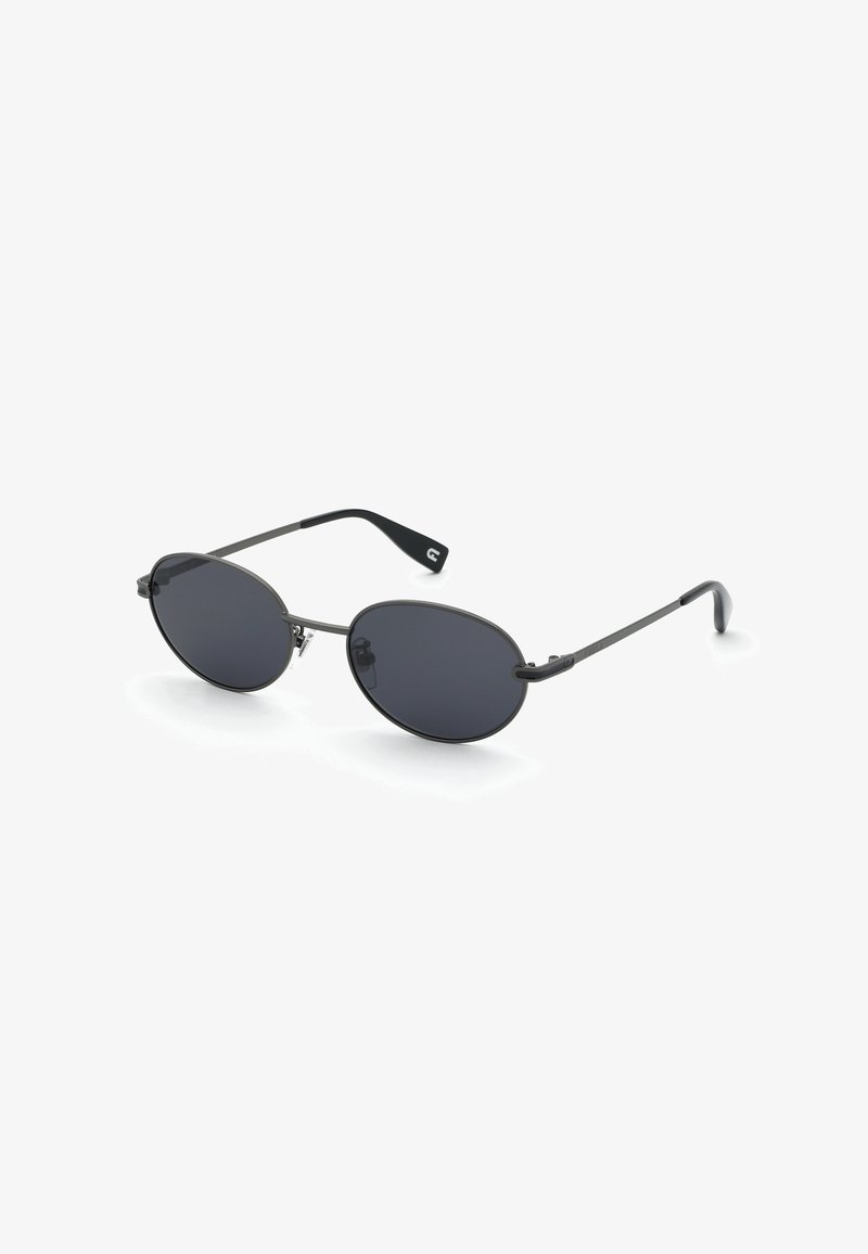 Lunettes de soleil ovales noires avec une fine monture métallique et des embouts de branches en plastique courbés sur fond blanc.