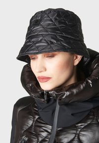 Cappello a secchio nero con una texture trapuntata, abbinato a un giubbotto imbottito con colletto alto e dettagli con zip, entrambi in materiali eleganti.
