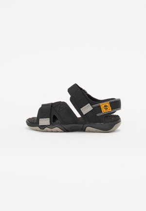Sandalias negras con correas ajustables, una suela texturizada y un parche de logotipo amarillo. Fabricadas con materiales sintéticos y un diseño deportivo.