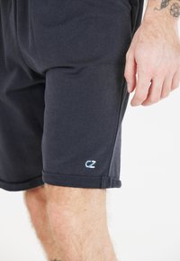 Miestne tmavomodré šortky vyrobené z bavlny, s manžetou na leme a malým svetlomodrým logom na dolnej ľavej nohe. Mäkka textúra.