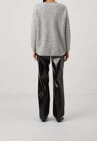 Grå stickad tröja med bred halsringning och långa ärmar, tillsammans med glänsande svarta vinylbyxor med vida ben. Inga tydliga mönster eller detaljer synliga.