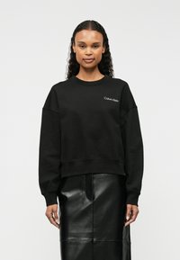 Μαύρο φούτερ από βαμβακερό μείγμα με στρογγυλή λαιμόκοψη και πτώσεις στους ώμους, με λευκό λογότυπο "Calvin Klein" στο αριστερό στήθος.