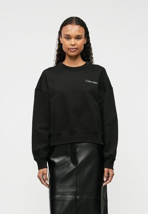Felpa nera in misto cotone con scollatura tonda e spalle scese, con il logo bianco "Calvin Klein" sul lato sinistro del petto.