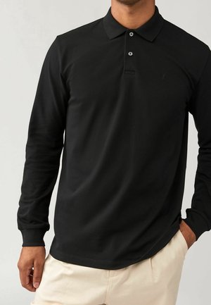 Polo-shirt noir à manches longues en tissu lisse, avec un col pointu, deux boutons et un petit logo sur la poitrine.