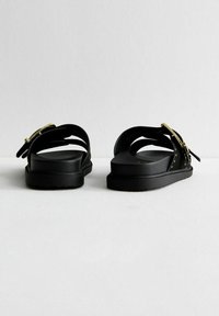 Sandales noires avec des sangles ajustables, boucles en ton doré, finition texturée et semelles plates. Présente un design minimaliste sans ornementation.