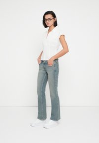 Λευκό κοντομάνικο πουκάμισο με κάθετες ρίγες και γιακά, συνδυασμένο με ανοιχτό μπλε τζιν παντελόνι καμπάνα και λευκά αθλητικά παπούτσια. Απλό, καθημερινό look.