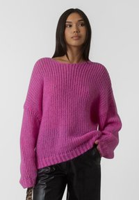 Maglione rosa oversize lavorato a maglia con scollo ampio, motivo a texture e maniche lunghe. Abbinato a pantaloni neri lucidi.