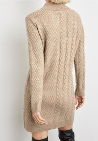 Robe pull beige en tricot avec un motif torsadé, des poignets côtelés et un col montant ; longueur mi-cuisse avec une silhouette ajustée.