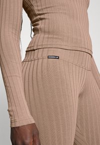 Brązowy prążkowany top z długim rękawem i dopasowane legginsy wykonane z elastycznego materiału. Na pasie wszyte logo NEBBIA. Faktura gładka.