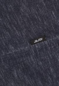 Donkerblauwe stof met een gestructureerde weving, voorzien van een klein zwart etiket met "J&Joy" in witte letters aan de rand.