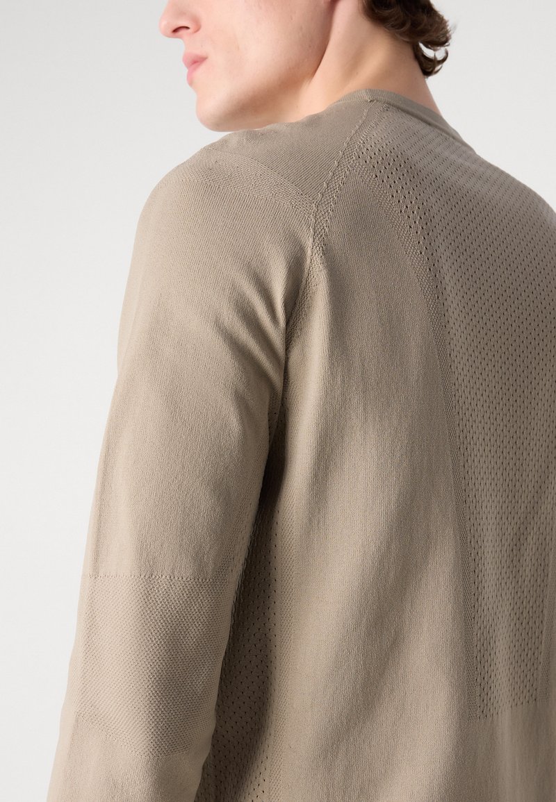 Camisa de manga larga color beige con un tejido de punto texturizado y paneles de malla sutiles, cuello redondo y silueta ajustada.
