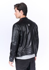 Giacca da motocicletta in pelle nera con dettagli trapuntati sulle spalle, texture a costine, design elegante e chiusura con zip ai polsini.